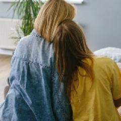 A child rests her head on a woman's shoulder 